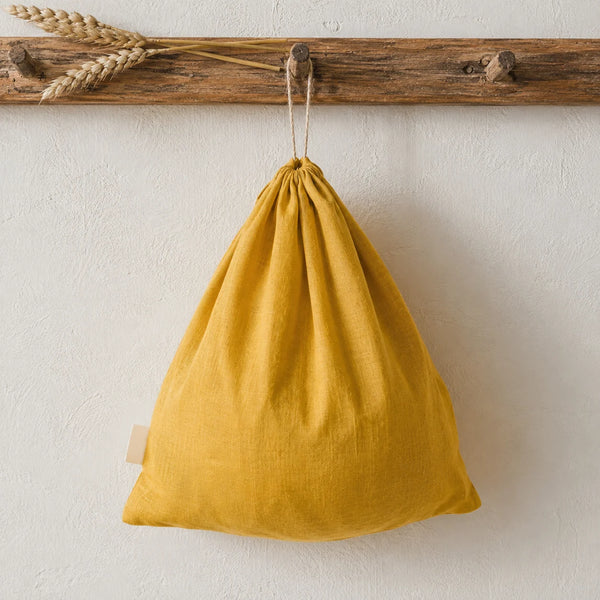 Mustard yellow linen loaf bag with drawstring hanging on a wooden peg rack