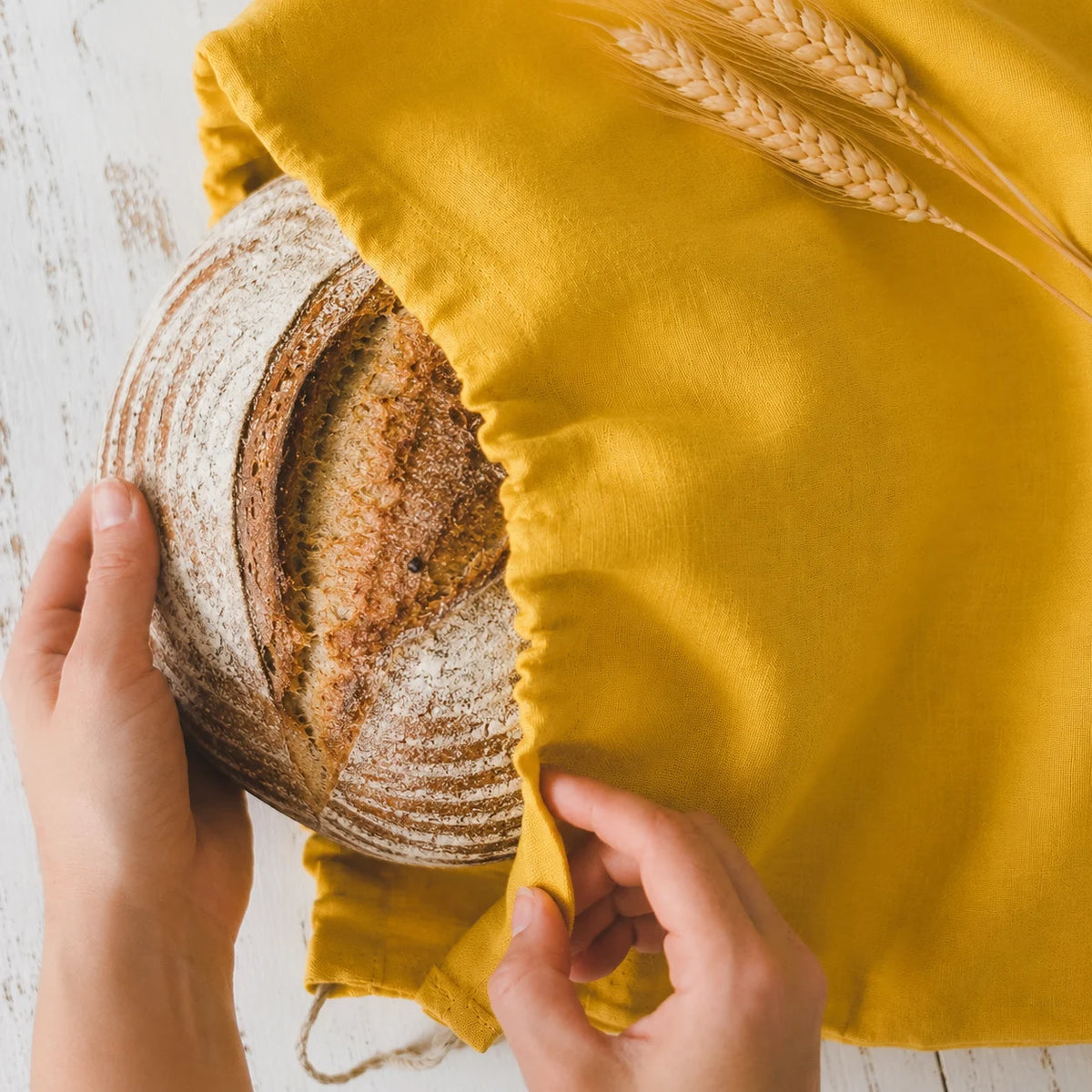 Hands lifting a fresh sourdough loaf out of the After Dough linen loaf bag